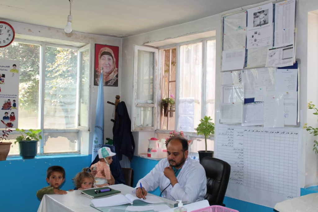 Male doctor at desk with two small children and a baby held by his mother