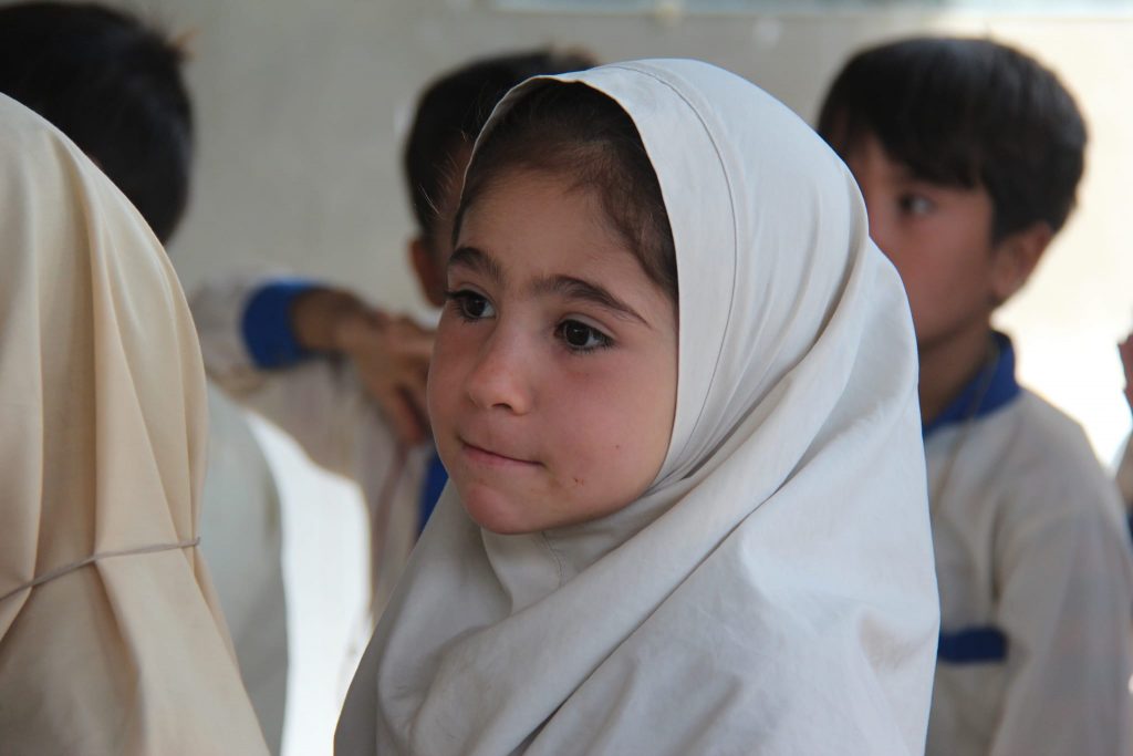 Little girl standing by other children in the background with a hijab