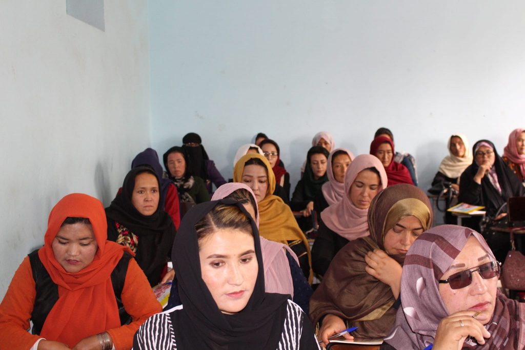 Women in class, at small desks with scarves of varying colors learning about health