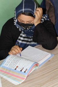 Woman in blue and white headscarf writing in a learning textbook